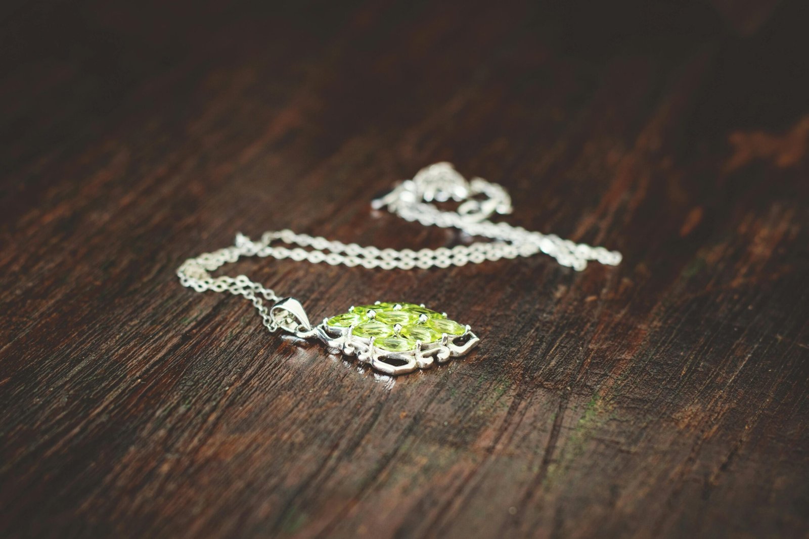 Close-up of a silver necklace featuring a green gemstone pendant on a rustic wooden surface.